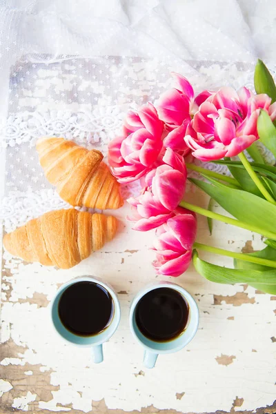 Nice cup of coffee, croissants and pink tulips on old white table, close-up — Stock Photo, Image