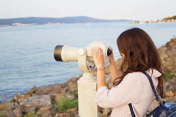 The girl looks through the telescope at the sea. — Stock Photo, Image