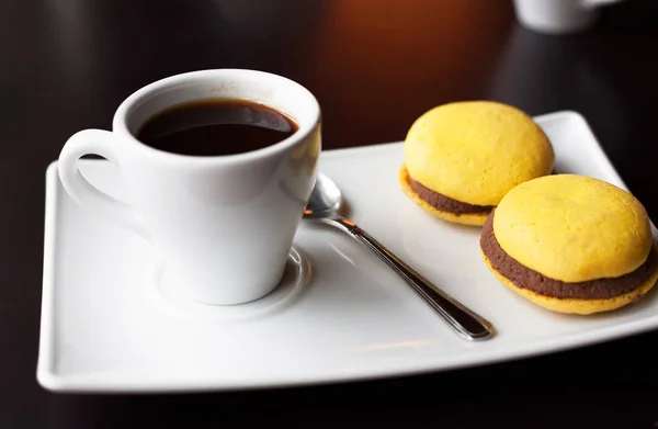 Une tasse de café noir et des macarons jaunes sur une assiette blanche — Photo