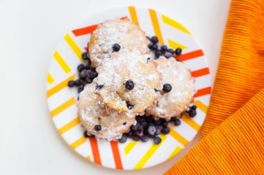 Peçetede yaban mersinli kek ve parlak turuncu tabak.