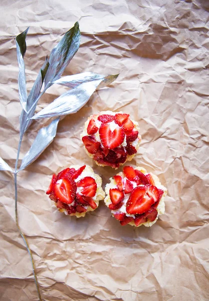 Beautiful cupcakes with strawberries along with a branch on kraft paper.