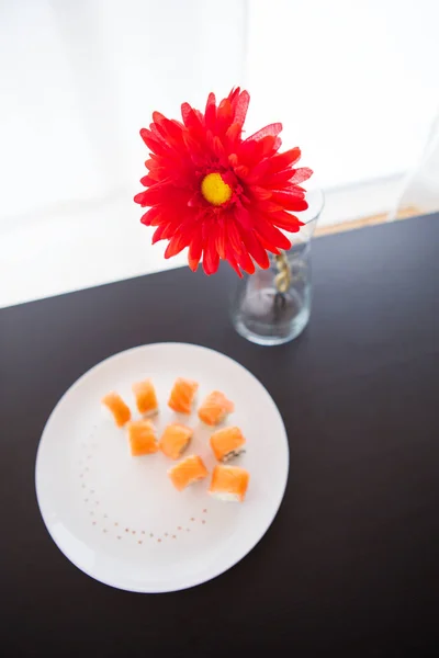 Sushi-Rolle mit Lachs, Philadelphia auf weißem Teller. rote Blume in einer Vase. — Stockfoto