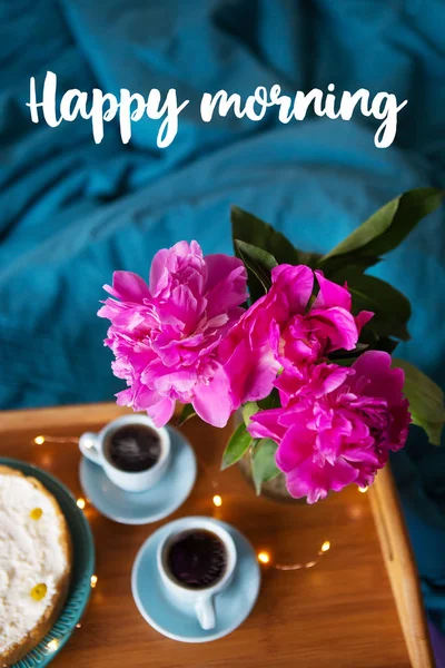 Koffie, roze Pioenen, kwarktaart op een houten dienblad, bovenaanzicht. Opschrift Happy Morning. — Stockfoto