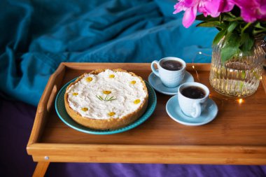 Yatakta kahvaltı. Pencere-şakayık, cheesecake ve ahşap bir tepsi üzerinde kahve iki fincan güzel ışık.