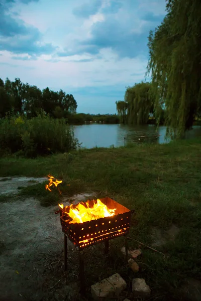 's avonds brandend brandhout in de grill, bereiding voor het bakken van vlees, bij het meer — Stockfoto