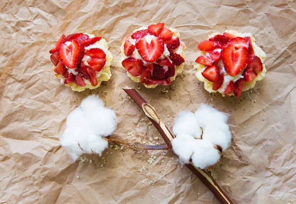 Schöne Cupcakes mit Erdbeeren zusammen mit einem Zweig Baumwolle liegt auf Kraftpapier — Stockfoto