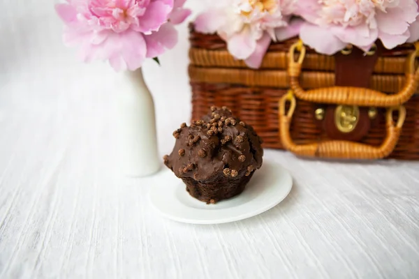 Chocolate muffins and beautiful pink peonies lie on a wooden suitcase. — Stock Photo, Image