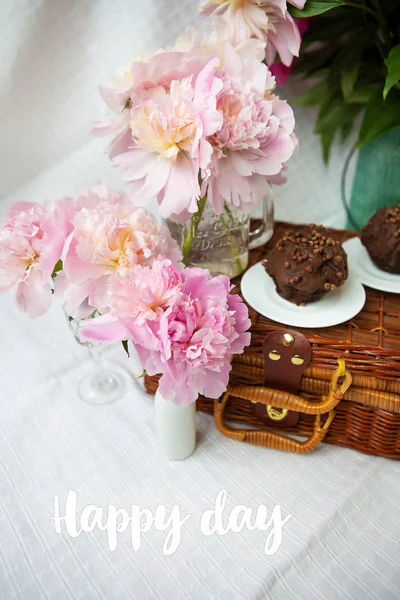 En mycket vacker bukett av rosa pioner i en vas står på en trä resväska. Inskription lycklig dag. — Stockfoto