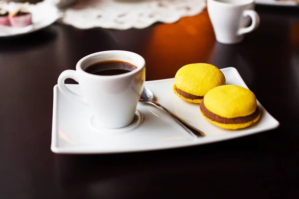 A cup of black coffee and yellow macaroons on a white plate — Stock Photo, Image