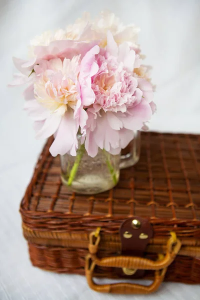 Дуже красивий букет з рожевих півоній у вазі стоїть на дерев'яній валізі . — стокове фото