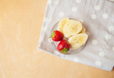 Ahşap bir zeminde cam bir tabakta çilek ve muz.