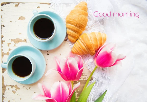 Mooie kop koffie, croissants en roze tulpen op oude witte tafel, het schrijven van goede morgen — Stockfoto