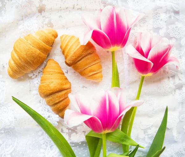 Three croissants and bright pink tulips on lace tablecloth — Stock Photo, Image