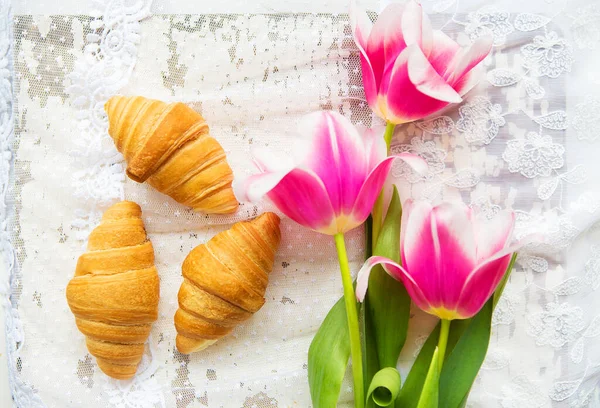 Three croissants and bright pink tulips on lace tablecloth, close-up — Stock Photo, Image