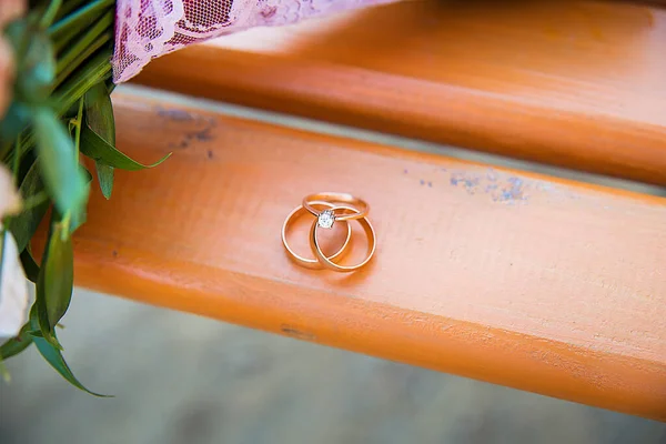 Három arany jegygyűrű egy fa padon. — Stock Fotó