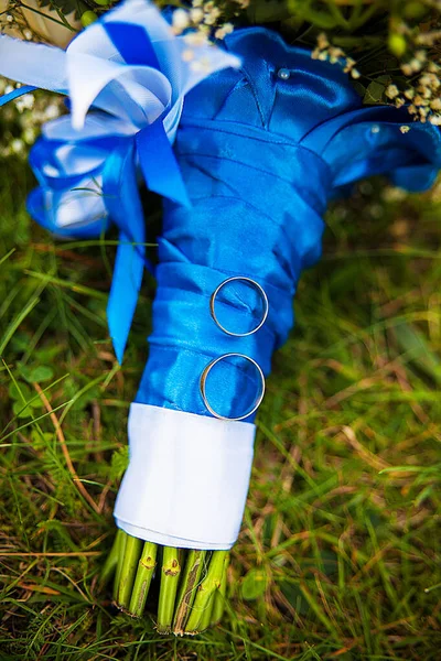 Snubní prsteny a svatební kytice ležící na zelené trávě — Stock fotografie