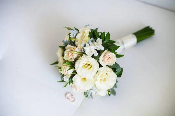 Bridal bouquet and rings lie on white sofa — Stock Photo, Image