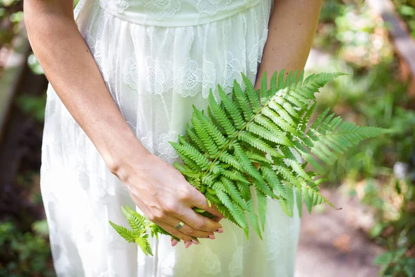 Flicka i en vit klänning, håller gröna ormbunksblad i skogen — Stockfoto