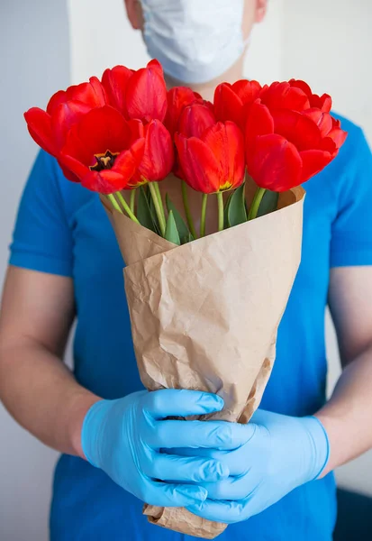 Contactless flower delivery by courier in a protective mask, medical gloves with a bouquet of red tulips. Close-up.