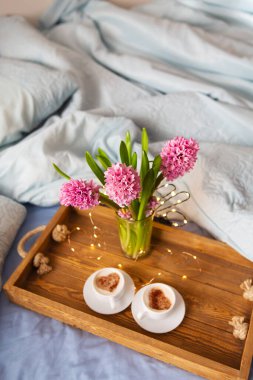 Bir buket güzel pembe sümbül vazonun içinde bir tepside duruyor, kalp desenli iki bardak kapuçino, yatakta sürpriz konsepti. Yazı için uygun bir yer. Yakın plan..