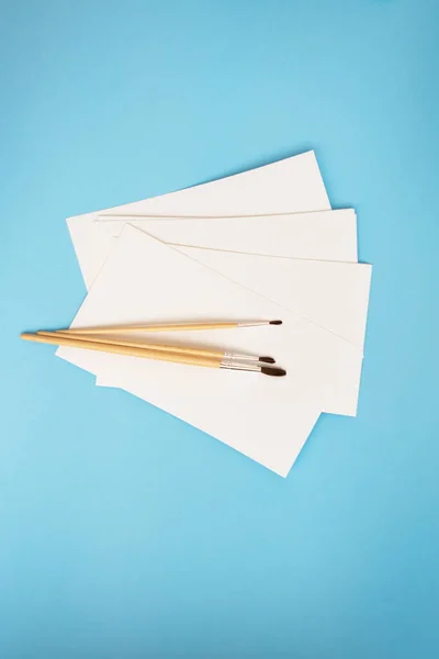 Pennelli ad acquerello di diverse dimensioni si trovano insieme con carta ad acquerello su uno sfondo blu. Lezioni di disegno. primo piano, vista dall'alto. — Foto Stock
