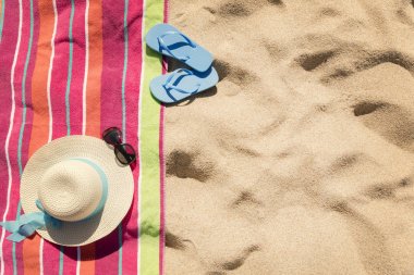 Kum üzerinde şapkalı plaj havlusu, güneş gözlüğü ve parmak arası terlik
