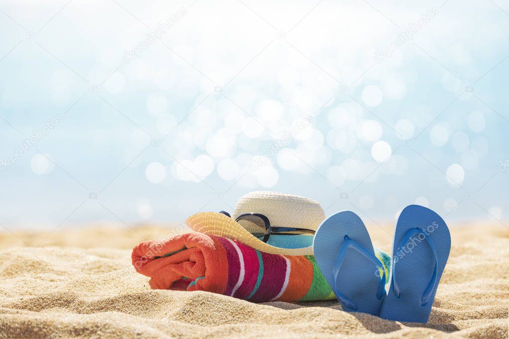 Beach accessories straw hat, flip flops, towel on sunny tropical beach, summer holidays