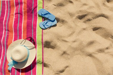 Kum üzerinde şapkalı plaj havlusu, güneş gözlüğü ve parmak arası terlik