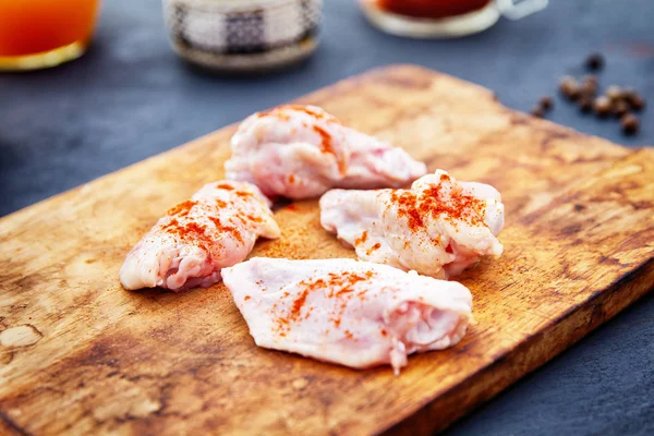 Alitas de pollo crudas con especias en una tabla de cortar de madera —  Fotos de Stock