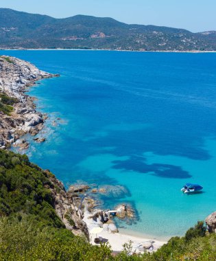 Akuamarin şeffaf su ve kayalık sahil kumlu plaj tekne ile yaz deniz sahne. Kıyıdan (Sithonia, Halkidikya, Yunanistan görüntülemek).