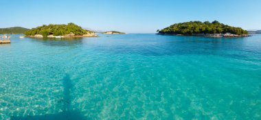 Beautiful Ionian Sea with clear turquoise water and morning summer coast view from beach (Ksamil, Albania). On water is the shadow of the photographer. clipart