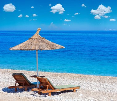 Yaz sabah çakıllı plaj şezlong ve saman tente (Arnavutluk) ile. Derin mavi gökyüzü ile aynı cumulus bulutları. İki tane dikiş yüksek çözünürlüklü görüntü.