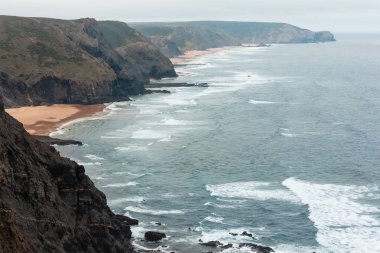 Sandy beach taşlı sırtlar ile hava görünümü yaz Atlantik kayalık kenarı (Costa Vicentina, Algarve, Portekiz) bulutlu. Ve okyanus sörf dalgalar.