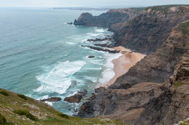 Sandy beach taşlı sırtlar ile hava görünümü yaz Atlantik kayalık kenarı (Costa Vicentina, Algarve, Portekiz) bulutlu. Ve okyanus sörf dalgalar.