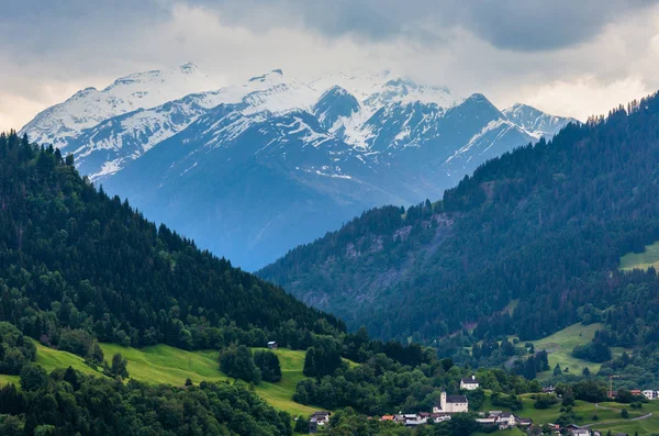 村と夏アルプスの山の風景 斜面のモミの森と雪が遠くに岩の頂上を覆った オーストリア — ストック写真