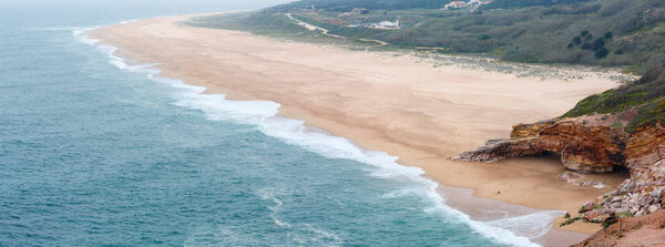 Sandy ocean beach near Nazare town (Portugal). Spring misty day. Panorama.