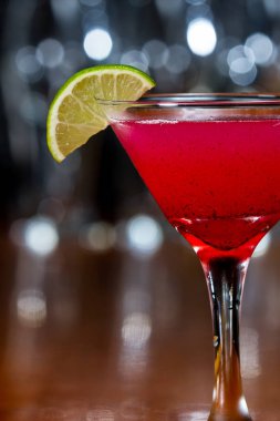 bir ahşap bar ayarı içinde limon dilimi ile süslenmiş bardağın dibinde yüzen küçük huckleberry tohumları ile kırmızı soğutulmuş martini