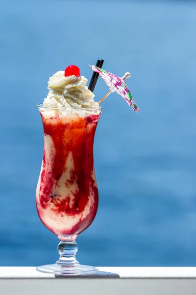 refreshing pina colada served with blended berries as a garnish and topped with whipped cream with a natural blue water background as a travel holiday concept