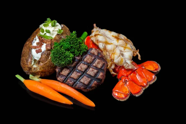 烤龙虾和菲力米格农配上装有的烤土豆和在黑色背景上隔离的蔬菜 — 图库照片