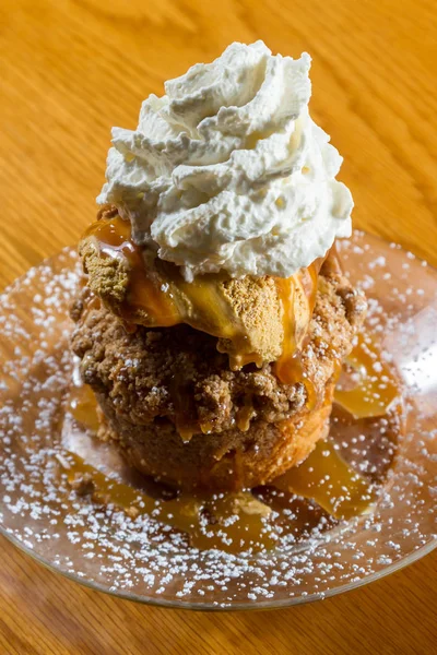 layered dessert consisting of an apple cake topped with salted caramel ice cream and a dollop of whipped cream