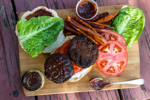 烤植物汉堡配上自制的酱汁和木制的切菜板上的新鲜番茄和生菜 — 图库照片