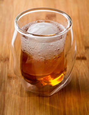 Whiskey soda served in a double walled whisky glass served with an ice sphere served on a wooden bar top clipart