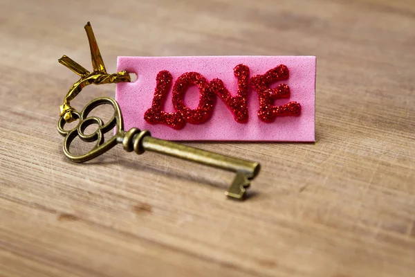 木製の背景に愛という言葉をスペル チェック赤キラキラ文字でピンクのタグが古いキーを使用して概念のイメージ — ストック写真
