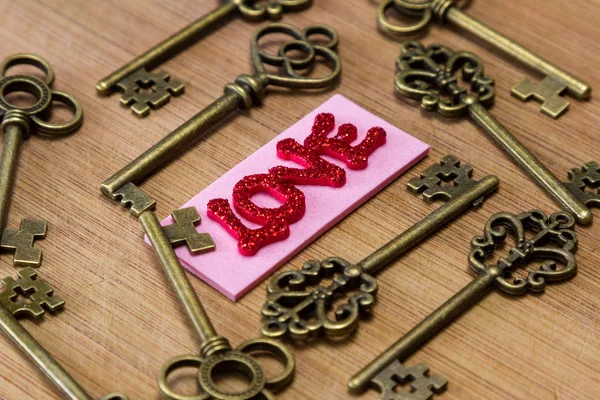 ピンクのタグが古いキーを用いた木製の背景に愛という言葉をスペル チェック赤キラキラ文字概念図 — ストック写真