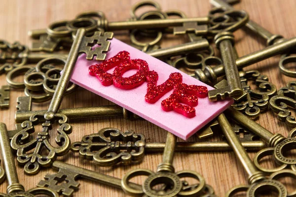 ピンクのタグが古いキーを用いた木製の背景に愛という言葉をスペル チェック赤キラキラ文字概念図 — ストック写真