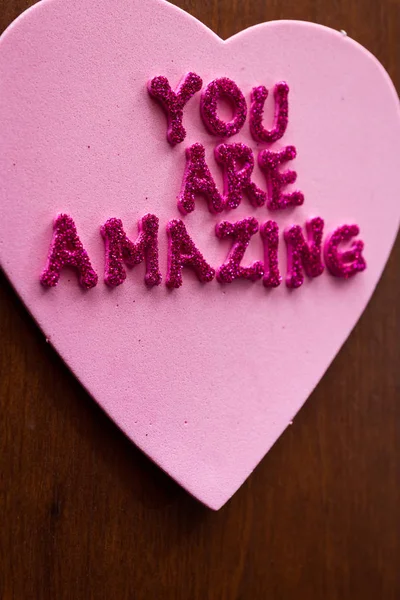 the words you are amazing in glitter letters on a pink heart stuck on a wooden cabinet