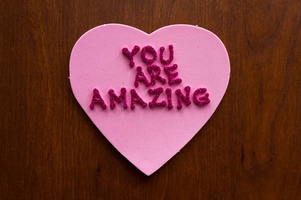 the words you are amazing in glitter letters on a pink heart stuck on a wooden cabinet