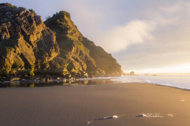 Güneş ufkun altına batarken Güney Oregon sahillerindeki manzaraya parlaklık ve renk katarken, altın ışık Cape Sebastian 'daki kayalara yansıyor.