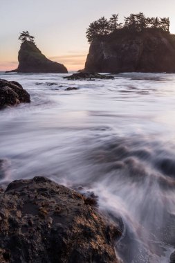Gün batımında Güney Oregon sahilindeki gizli sahilde güneş batıyor. Dalgalar değiştikçe dalgalar bulanıklaşıyor.
