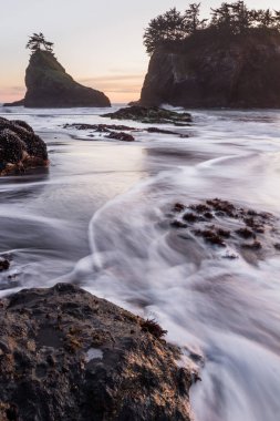 Gün batımında Güney Oregon sahilindeki gizli sahilde güneş batıyor. Dalgalar değiştikçe dalgalar bulanıklaşıyor.